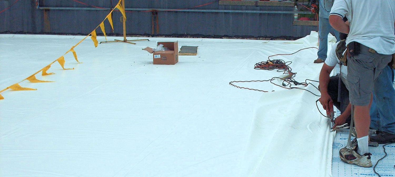 Crew installing a white single-ply membrane on a commercial flat roof
